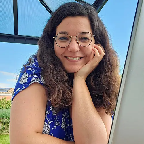 Femme souriante avec des lunettes et une robe bleue à motifs.