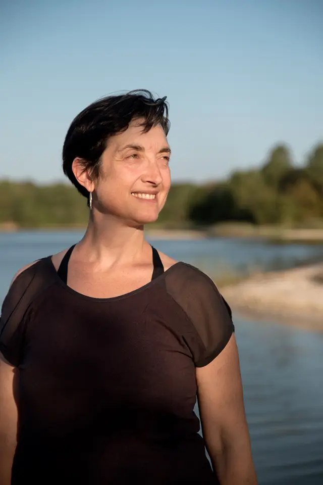 Isabelle Bertone, coach en évolution financière, souriante près de l'eau, symbolisant la sérénité et l'accomplissement personnel.