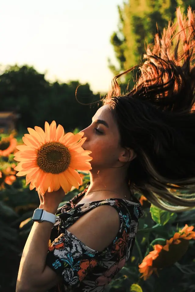 Femme en robe rouge dans un champ de tournesols, levant les bras et lançant un chapeau en l'air, symbolisant l'argent comme allié pour l'accomplissement personnel.